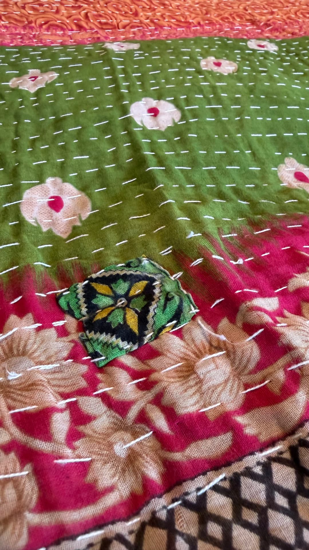 A small dark floral patch stitched over green and magenta Kantha cloth — a visible repair