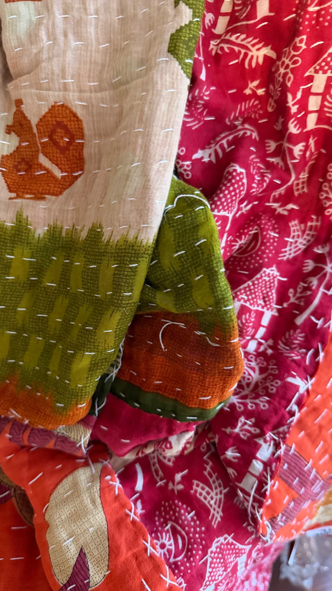 Draped Kantha quilts in green, magenta, and orange, the running stitches catching the light along the folds