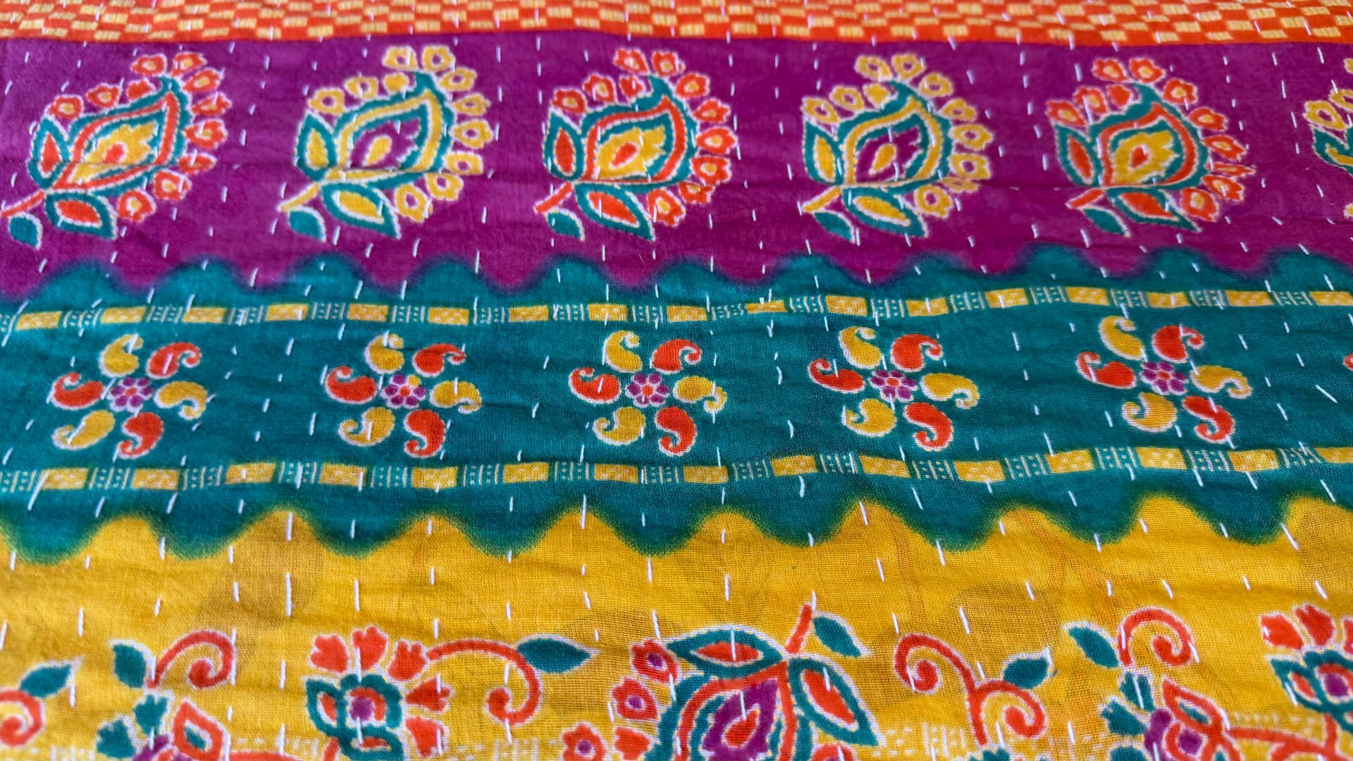 Vivid bands of magenta, teal, and yellow Kantha cloth with floral motifs and rows of white running stitch