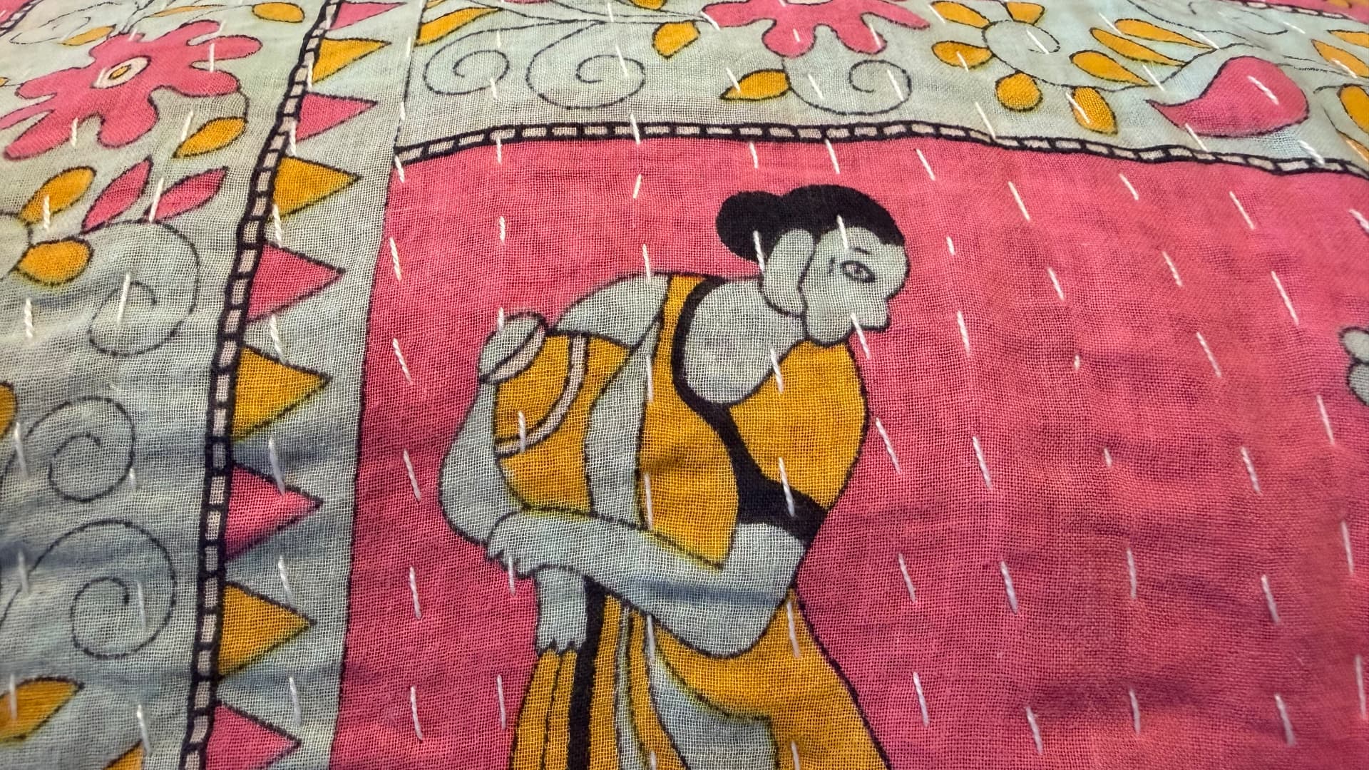 Close-up of a Kantha quilt — a printed figure of a woman carrying a vessel, crossed by rows of white running stitches