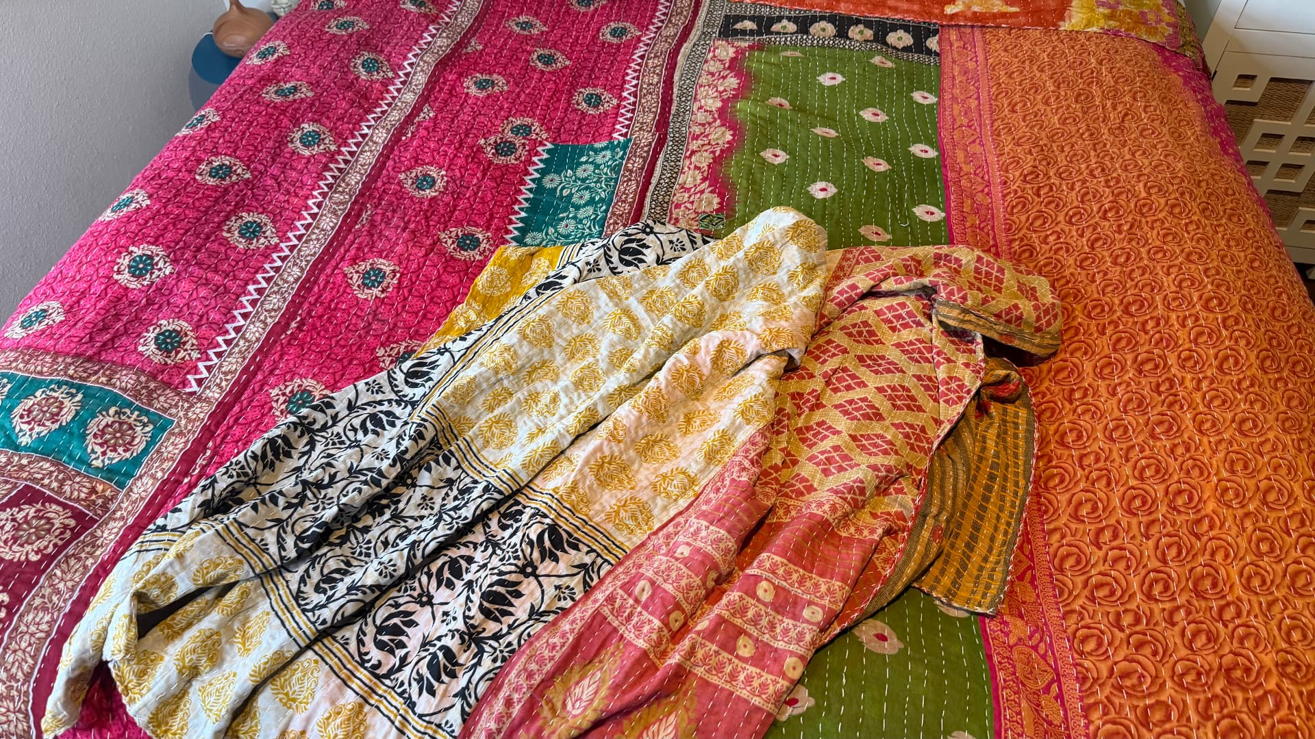 Several Kantha quilts spread across a bed — magenta, green, orange, and black-and-white prints overlapping