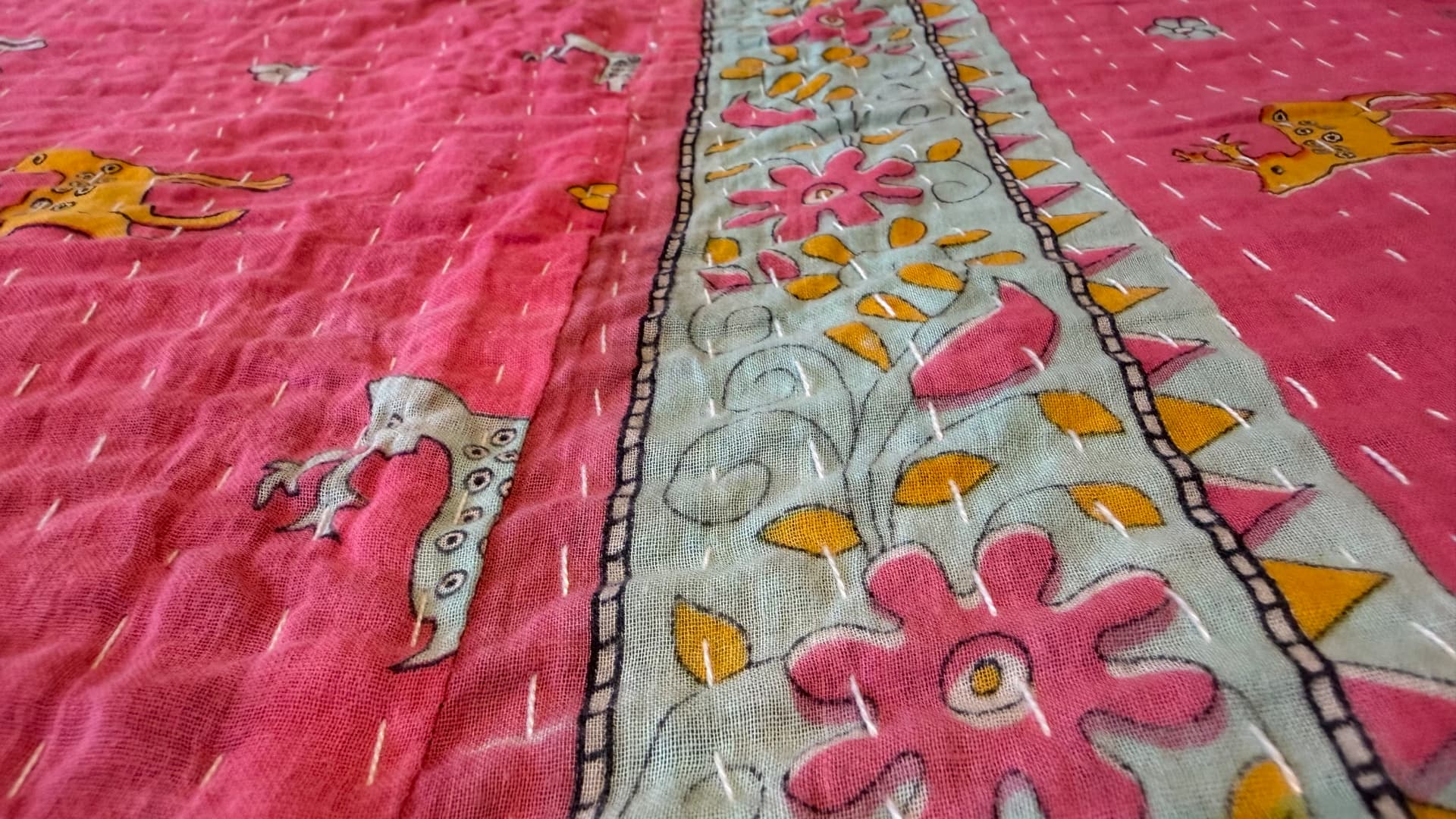 A field of pink Kantha cloth patterned with small deer, crossed by a floral vine border