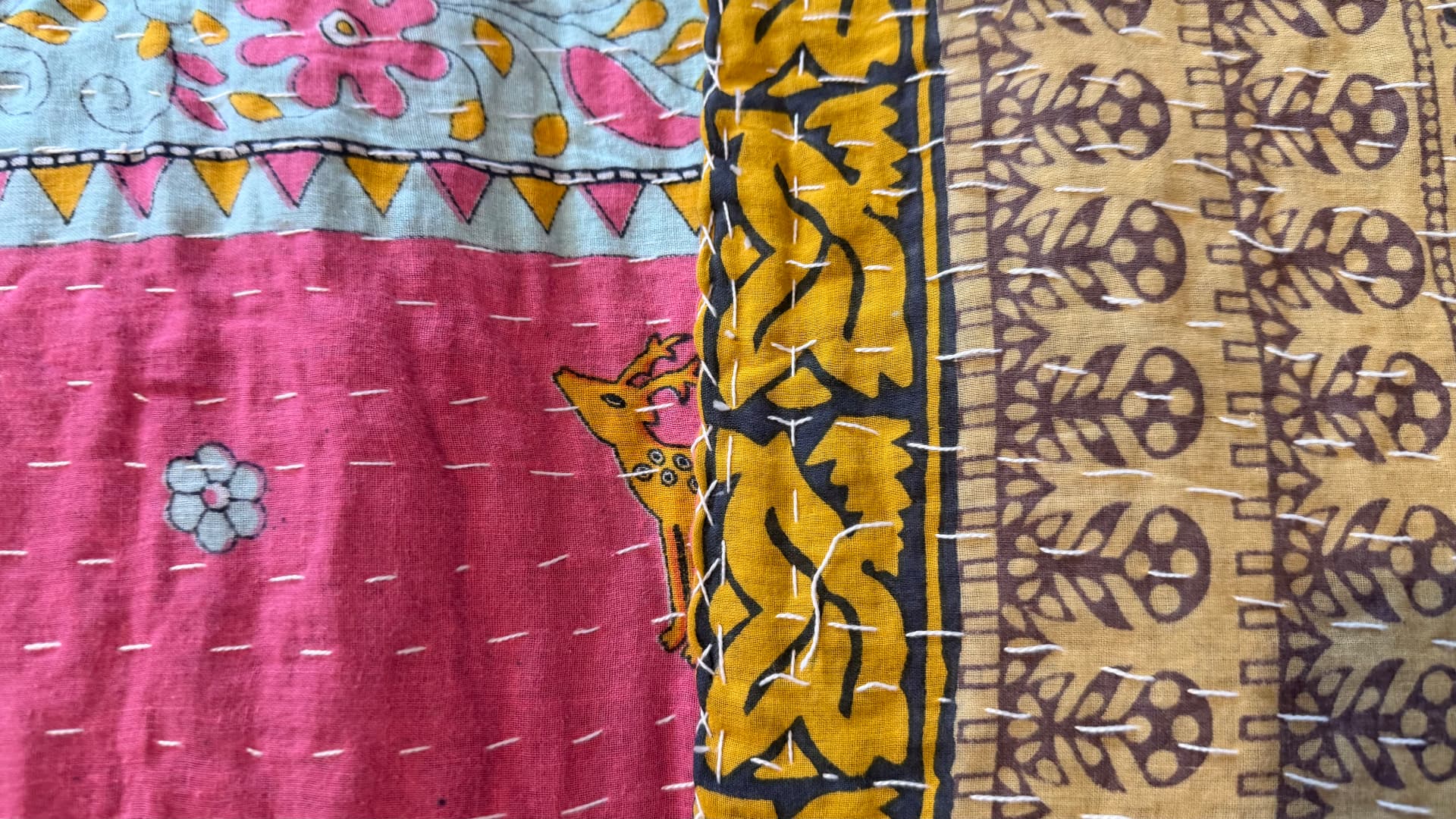 Kantha cloth showing a printed deer beside bands of yellow leaf and beige vine patterns, all crossed by running stitches