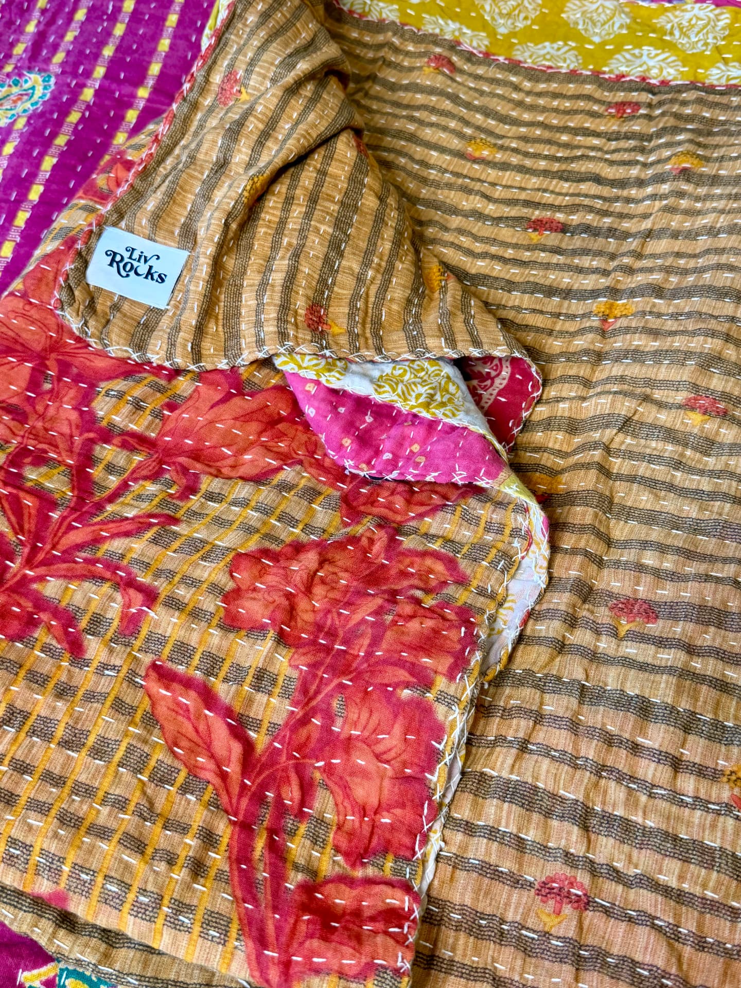 A folded Kantha quilt in tan stripes and red florals, bearing a small LivRocks label
